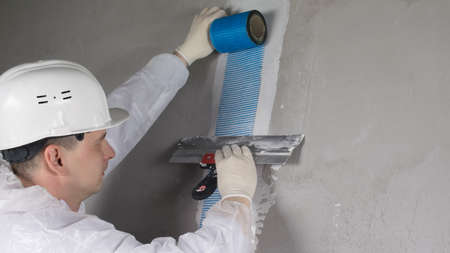 a worker in special clothes and a helmet glues the wall joint with a blue mesh, repairの写真素材