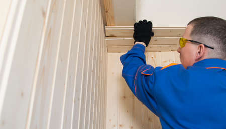 master in a blue uniform and yellow glasses, closes the ceiling of a small room with natural wood, a...