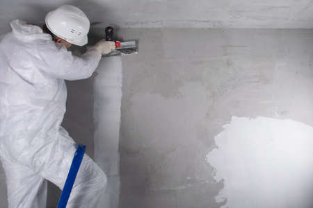 a master in a protective uniform and a white helmet, closes a crack in the wall with a white...