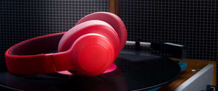 red headphones lie on a turntable, against the background of old speakers, close-up