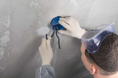 man in safety glasses installs an electrical outlet into the wall, rear view