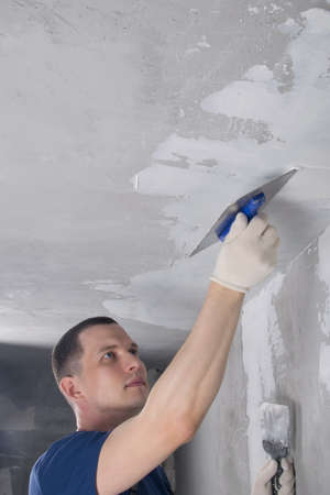 master in protective gloves for repairing concrete walls, aligns the ceiling with a spatulaの写真素材
