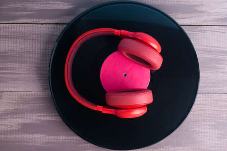 on a painted wooden background, lies a black vinyl record with bright red headphones on itの写真素材
