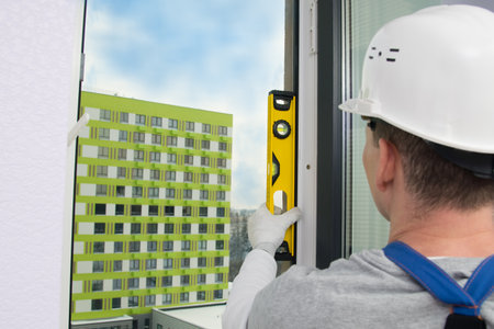 a construction worker in a white helmet, against the background of the sky and a residential building, checks the correct installation of the window, level, rear viewの写真素材