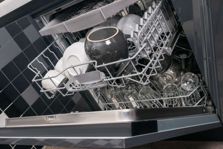 a stack of dirty dishes stands on the door of the dishwasher, front viewの写真素材