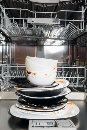 a stack of dirty dishes stands on the door of the dishwasher, front viewの写真素材
