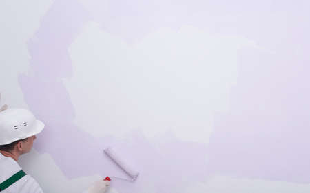 on a large light wall, there is a white spot for advertising, a worker paints the wallの写真素材