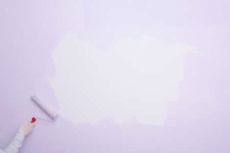 on a large light wall, there is a white spot for advertising, a worker's hand paints the wallの写真素材
