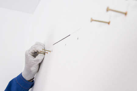 a hand in a protective glove holds the self-tapping screw in the dowels before twistingの写真素材
