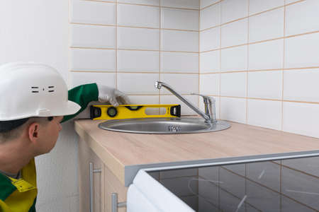 the carpenter checks the correct installation of the countertop on the kitchen furnitureの写真素材