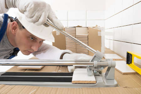 a worker makes a cut of a ceramic tile with a special tool, side view