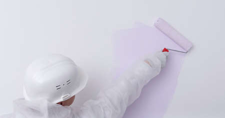 painter in protective clothing and hard hat, applies paint to the wall, rollerの写真素材