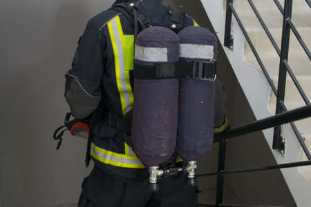 a firefighter with a breathing apparatus, in the form of two cylinders on his back, goes down the smoke-free stairs to check the lower floorsの写真素材