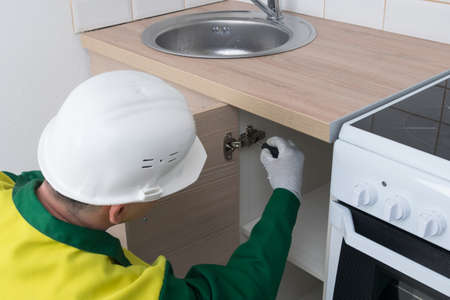 a master in a white protective helmet for the assembly of kitchen furniture, installs the hinges of the hinged doorの写真素材