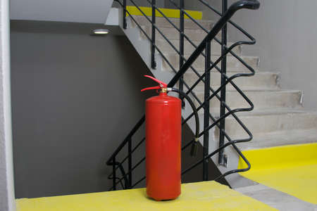 a red large fire extinguisher stands on the landing of the stairwell for safe evacuation in case of fireの写真素材