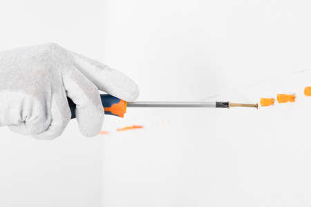 hand with a screwdriver twists a self-tapping screw into a white concrete wall, close-upの写真素材