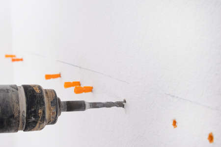 a hammer drill makes a hole in a white concrete wall, close-upの写真素材