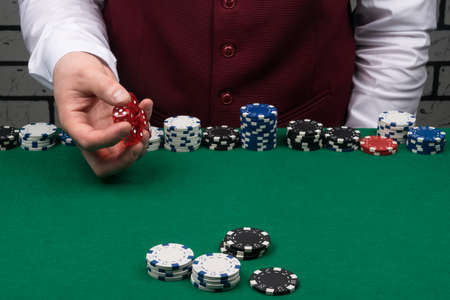 the croupier's hand is holding red dice over the green cloth of the poker tableの写真素材