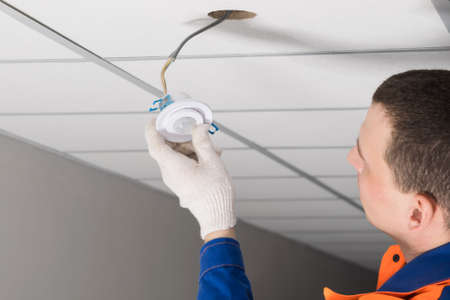 a worker installs lighting equipment into the false ceilingの写真素材