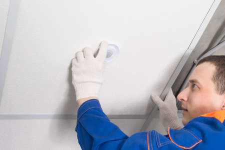a worker adjusts a lamp in a false ceiling, close-upの写真素材