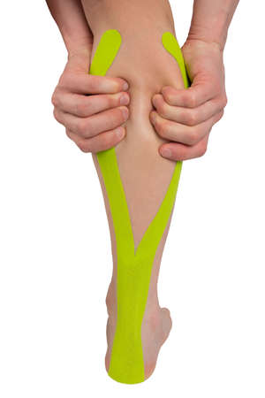 on a white background, a close-up of a leg with a taped tape, for recovery from a sports injury, and two hands clasping the calf partの写真素材