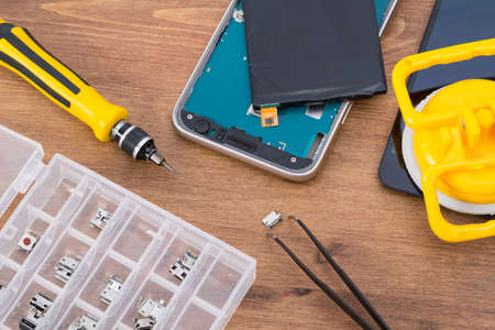 on the wooden table, spare parts to replace the smartphone charging connector, tweezers and glass to replaceの写真素材