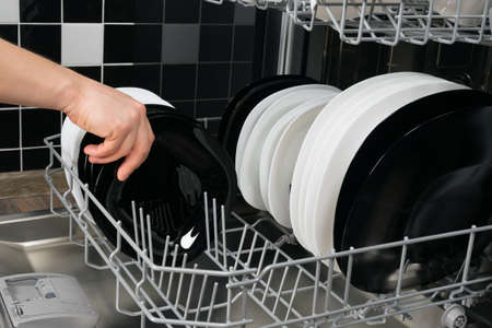 against the background of a black and white kitchen, a man's hand pulls a clean plate out of the dishwasherの写真素材