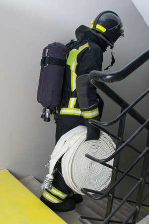 a firefighter in black protective clothing carries equipment to fight the fire on the evacuation ladderの写真素材