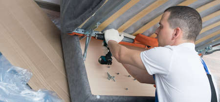 master in the Assembly and repair of upholstered furniture, twists the sofa with a screwdriver, close-upの写真素材