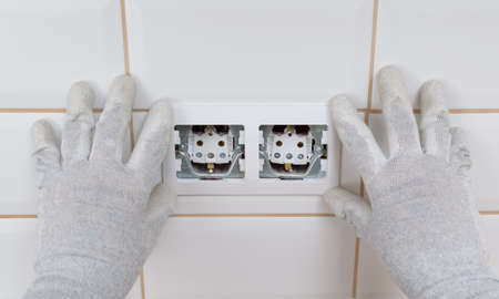 close-up of two hands in protective gloves, installing an electrical outlet, on a light white tileの写真素材