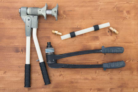 on the wooden surface, there is an expander for plastic pipes, a press for water supplyの写真素材