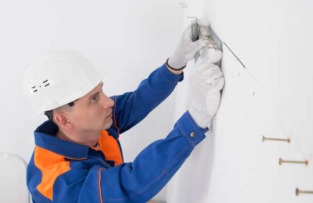 a worker in a protective helmet, on a white wall, sets a bar for fixing hanging cabinets of kitchen furniture, close-upの写真素材