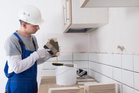 the master of laying tiles, takes a mixture for gluing finishing materials to the wall, a man in a hard hatの写真素材