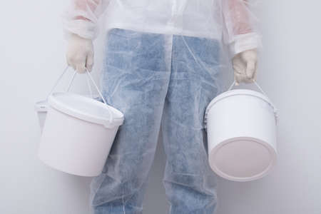 a man in protective clothing, bringing buckets of paint, against a white wall, close-upの写真素材