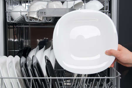 against the background of the dishwasher is a white plate with a place for writing in a man's handの写真素材