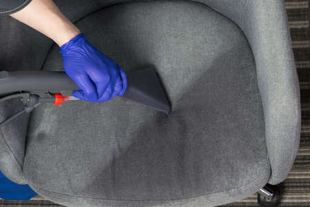 cleaning specialist in protective clothing, collects water with cleaning agent from the drapery of the chair, vacuum cleanerの写真素材