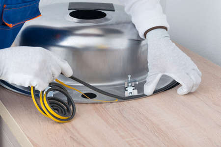 a specialist in protective clothing, glues a sealing tape to eliminate moisture between the countertop and the metal sinkの写真素材