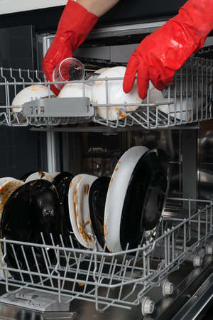hands in red protective gloves, cleaning plates of large food debris, for putting in the dishwasherの写真素材