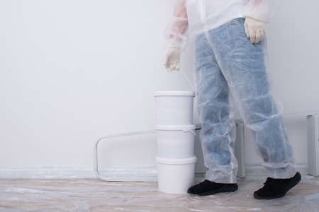 a man in protective clothing, brings buckets of paint and a set of tools, against the background of a white wall, there is a place for the inscriptionの写真素材