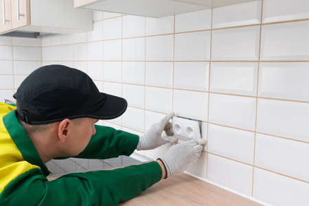 the electrician installs a double socket for household appliances on the facade of the tile, close-up, there is a place for the inscription on topの写真素材