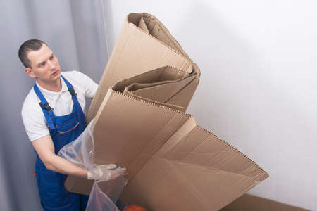 a male loader, after delivering furniture, takes out a cardboard package for recyclingの写真素材