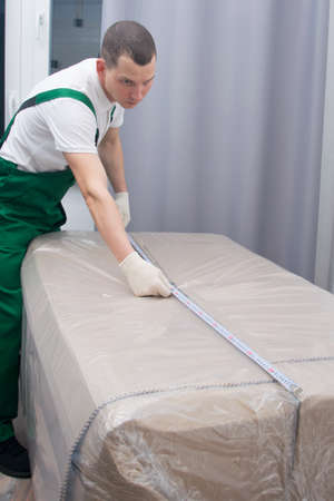 the loader is a man, measuring the dimensions of a large box, for moving into the doorwayの写真素材