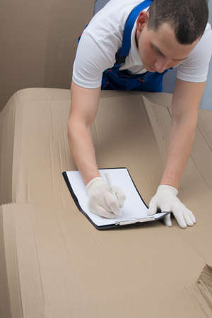 against the background of a large cardboard box, a loader in protective gloves fills out the documents for the goodsの写真素材