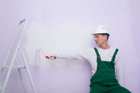 a construction worker in protective clothing, holding out his hands with a roller for applying paint to the wallの写真素材