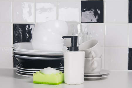 on the table, against the background of black and white tiles, washed dishes, plates, mugs, and on the sponge foam for disinfectionの写真素材