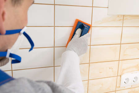 the master rubs the brown grout on white tiles with a special sponge, finishing workの写真素材