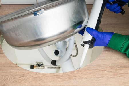 a worker smears the edges of the hole with liquid glue to install the sink in the kitchen countertop, close-upの写真素材