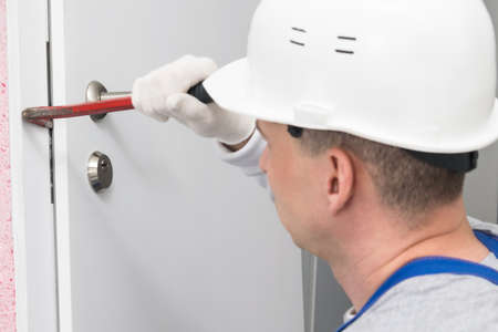 a construction worker in a helmet opens the front door with a special toolの写真素材
