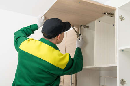 a furniture assembler adjusts the closing mechanism of the kitchen cabinetの写真素材