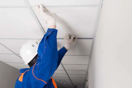 a worker in a helmet is installing a suspended ceiling, rear viewの写真素材